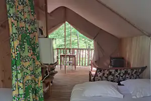Zeltterrasse mit Holzboden, Tisch und Stühlen, Vorhangmuster an der Wand und Blick durch die Tür in den Garten.