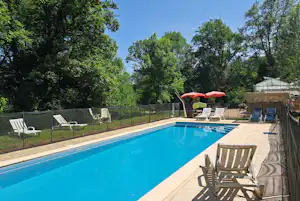 Blauer Pool auf der Terrasse mit Liegestühlen, Sonnenschirm und Blick in den grünen Wald.
