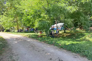 Campingplatz im Grünen mit mehreren Zelten, Campingstühlen und einem kleinen Holztisch zwischen Bäumen.