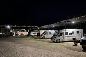 Wohnmobile und ein Zelt auf einem Campingplatz am Abend, beleuchtete Stellplätze und Wege zwischen den Fahrzeugen.