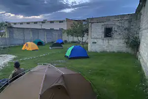 Campingzelt im Vordergrund auf grünem Rasen, daneben mehrere Zelte im Innenhof zwischen Steinmauern und Bäumen.