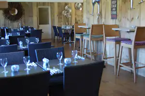 Essbereich im Campinghaus mit Holzwänden, gedeckten Tischen, Stühlen und Gläsern, im Hintergrund eine Tür und Deko.