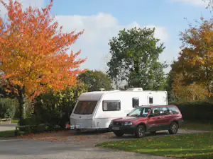 Wohnmobil und roter Pkw stehen auf einem Campingplatz am Rand eines Weges, umgeben von bunten Bäumen.