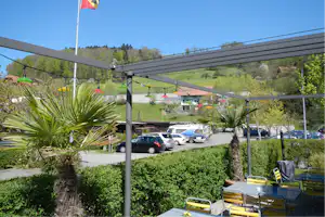 Blick vom Balkon auf den Campingplatz: Parkplatz mit Autos und Wohnmobilen, grüne Wiese und bunte Lampen unter dem Dach.