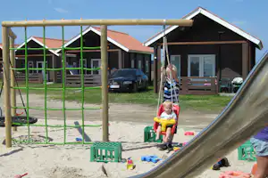 Camping Thorsminde - Kinder auf dem Spielplatz vom Campingplatz, Mobilheime mit Veranda im Hintergrund