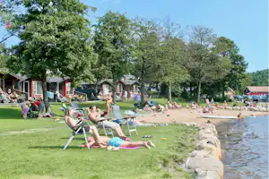 Campingplatz am Fluss mit Liegen auf der Wiese, Bungalows und Bäume am Ufer.