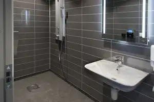 Modernes Camping-Badezimmer mit Dusche, Duschkopf, Waschbecken und Spiegel an grauen Fliesenwänden.