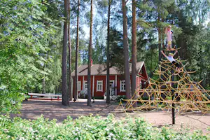 Seil-Klettergerüst auf dem Campingplatz vor einem Gebäude, umgeben von hohen Bäumen und Wegen.