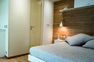 Modernes Schlafzimmer mit Doppelbett, Holzverkleidung und Nachttischlampe, daneben eine Tür und Schrankfronten im Bungalow.