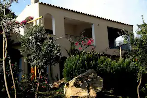 Ferienhaus mit Terrasse, Balkon und Zierpflanzen im Garten, Steinweg und Sträucher vor dem Gebäude.