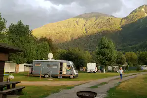 Wohnmobil auf dem Campingplatz, im Hintergrund bewaldete Berge und Bäume, daneben ein weiteres Fahrzeug und Fahrräder.