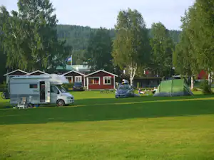 Wohnwagen und Mobilheime auf einem Campingplatz, daneben ein Zelt und ein Auto auf der grünen Wiese.