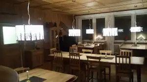 Holz-Essbereich im Campinghaus mit mehreren Tischen und Stühlen, großen Fenstern und Lampen an der Decke.