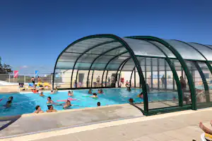 Beheiztes Schwimmbecken mit Menschen im Wasser und einem großen Glasdach über dem Pool, daneben Liegeflächen.
