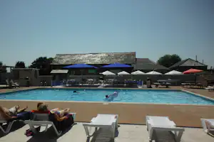 Camping-Pool mit blauem Wasser, Sonnenliegen auf der Terrasse und Zeltüberdachungen im Hintergrund.