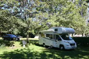 Wohnmobil auf einem Campingplatz im Grünen, mit Auto daneben und Bäumen im Hintergrund.