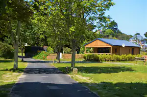 Holzbungalow mit Schiebetür und Terrasse, daneben ein gepflasterter Weg durch den grünen Garten mit Bäumen.