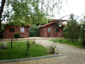 Holz-Bungalows auf einem Campingplatz, mit Kiesweg, Rasen und Bäumen im Vordergrund.