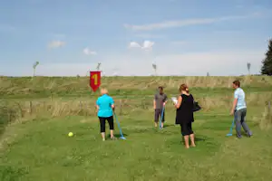 Golfspiel auf einer grünen Wiese am Campingplatz, mit Schild „1“ und Spielern mit Schlägern.