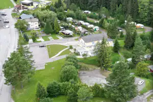 Luftaufnahme einer Campinganlage mit vielen Stellplätzen, Rasenflächen, kleinen Hütten und Wohngebäuden inmitten von Bäumen.