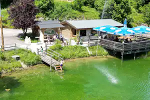 Holzsteg am grünen Teich vor Campinghütten, im Hintergrund Zelte mit Pontigamer-Banner und Sitzbereich.