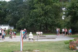 Campingplatz mit Wohnwagen-Stellplatz, Grillbereich und Bank, im Hintergrund Bungalows und viel Grün im Park.