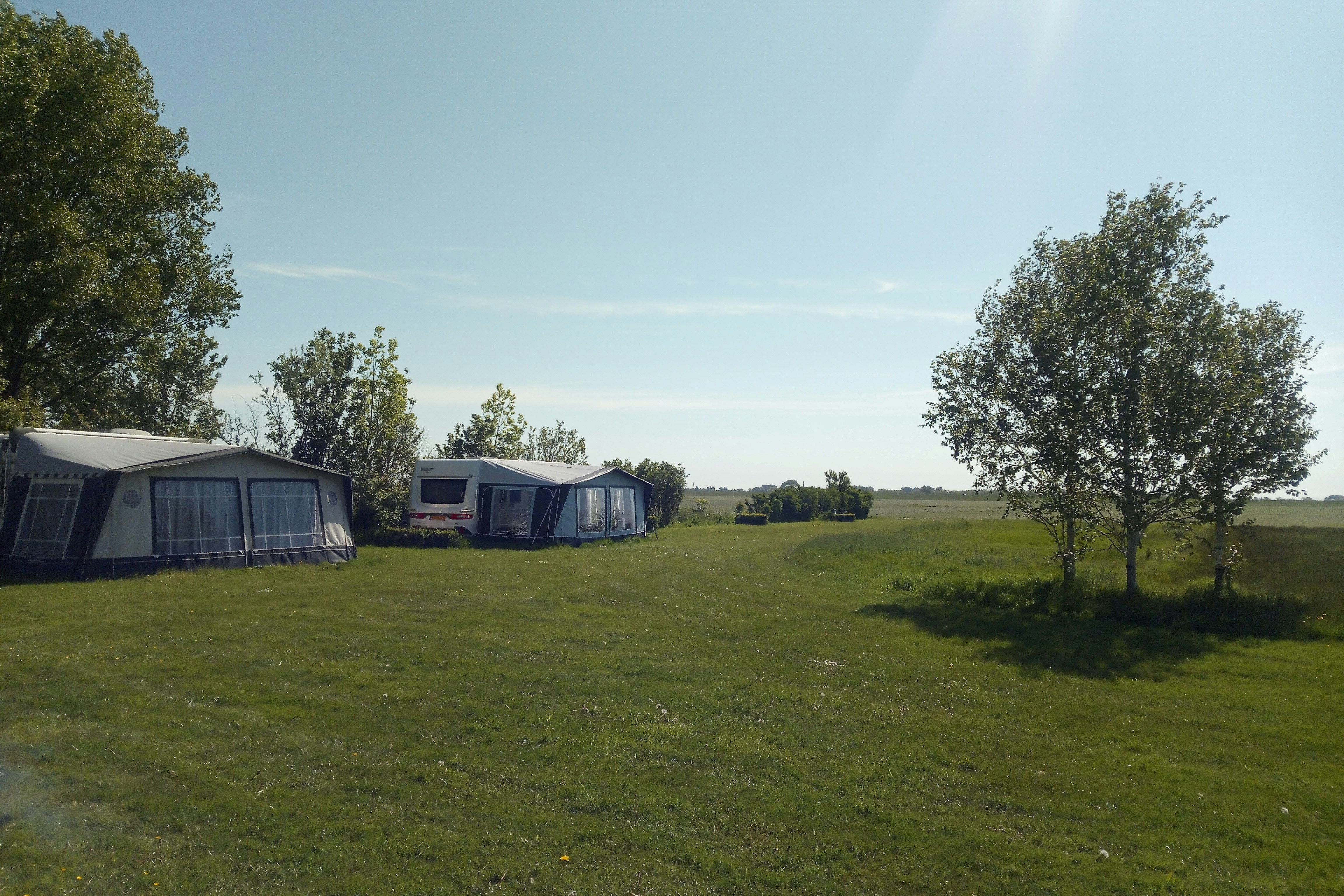 Campingzelte und Wohnwagen auf einer grünen Wiese, mit Bäumen und freiem Blick in die Landschaft.