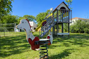 Spielgerät für Kinder mit Federwippe auf dem Campingplatz, im Hintergrund Zäune und ein Gebäude mit Terrasse.