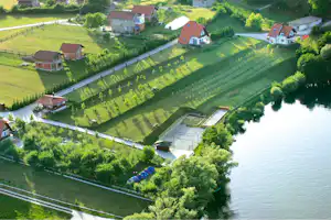 Campingplatz am See mit mehreren Häusern, gepflegten Wegen, Rasenflächen und einem kleinen Steg am Ufer.