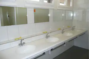 Gemeinschaftsbad mit langen Waschtischen, Waschbecken, Armaturen und Spiegeln über den Fliesenwänden.