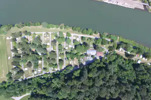 Luftaufnahme eines Campingplatzes am Fluss mit vielen Stellplätzen, Wegen, Gebäuden und viel Grün im Hintergrund.