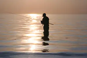 Stand-up-Paddler auf einem See bei Sonnenuntergang, Silhouette auf dem Wasser mit spiegelnden Lichtreflexen.