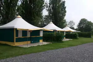 Großes Campingzelt mit Vorhang und Markise auf einem Stellplatz, neben Gras und Bäumen am Weg.