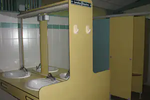 Camping-Badezimmer mit zwei Waschbecken, Armaturen und gelben Toilettenkabinen mit Türen.