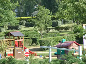 Wohnwagen-Stellplatz auf einem Campingplatz im Grünen, mit Hecken, Bäumen, Wegen und einem kleinen Holzunterstand.