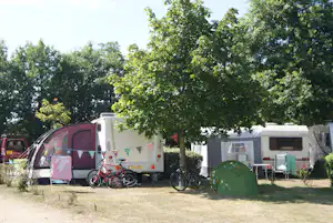 Wohnwagen und Zelt auf einem Campingplatz, daneben Fahrräder und Campingstühle unter Bäumen.
