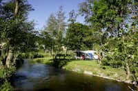 Camping Val d'Or - Wohnwagen zwischen Bäumen am Ufer des Flusses