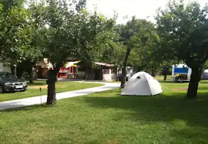 Zelt auf einem gepflegten Campingplatz mit Rasen, Kiesweg und Bäumen; im Hintergrund Wohnwagen und Gebäude.