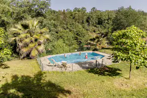 Camping-Pool im Grünen mit Liegen und Zaun, umgeben von Bäumen und Sträuchern.