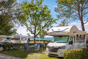 Wohnmobil auf dem Stellplatz mit Markise, Campingstühlen und Fahrrädern im Grünen, daneben weitere Wohnmobile und Bäume.