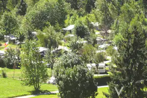 Campingplatz im Grünen mit Wohnwagen und Zelten zwischen Bäumen, Rasenflächen und Wegen im Hintergrund.