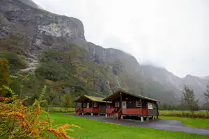 Mehrere Ferienhäuser am Campingplatz mit Holzfassaden, Parkplatz und Rasen im Tal vor hohen Bergen.