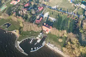 Luftaufnahme eines Campingplatzes mit Stellplätzen, Rundbecken, Fluss und Wegen, umgeben von Wiesen und Bäumen.