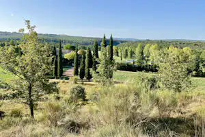 Blick über einen Campingplatz mit Olivenbäumen, Zypressen und Wegen durch das grüne Tal.