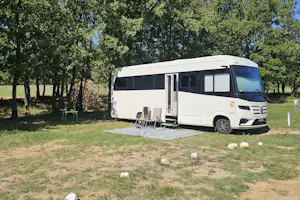 Wohnmobil auf einem Campingplatz am Grasplatz, mit Tisch und Stühlen neben dem Fahrzeug und Bäumen im Hintergrund.
