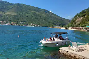 Boot am Steg am See, Campingbereich mit Liegestühlen und Blick auf bewaldete Berge im Hintergrund.