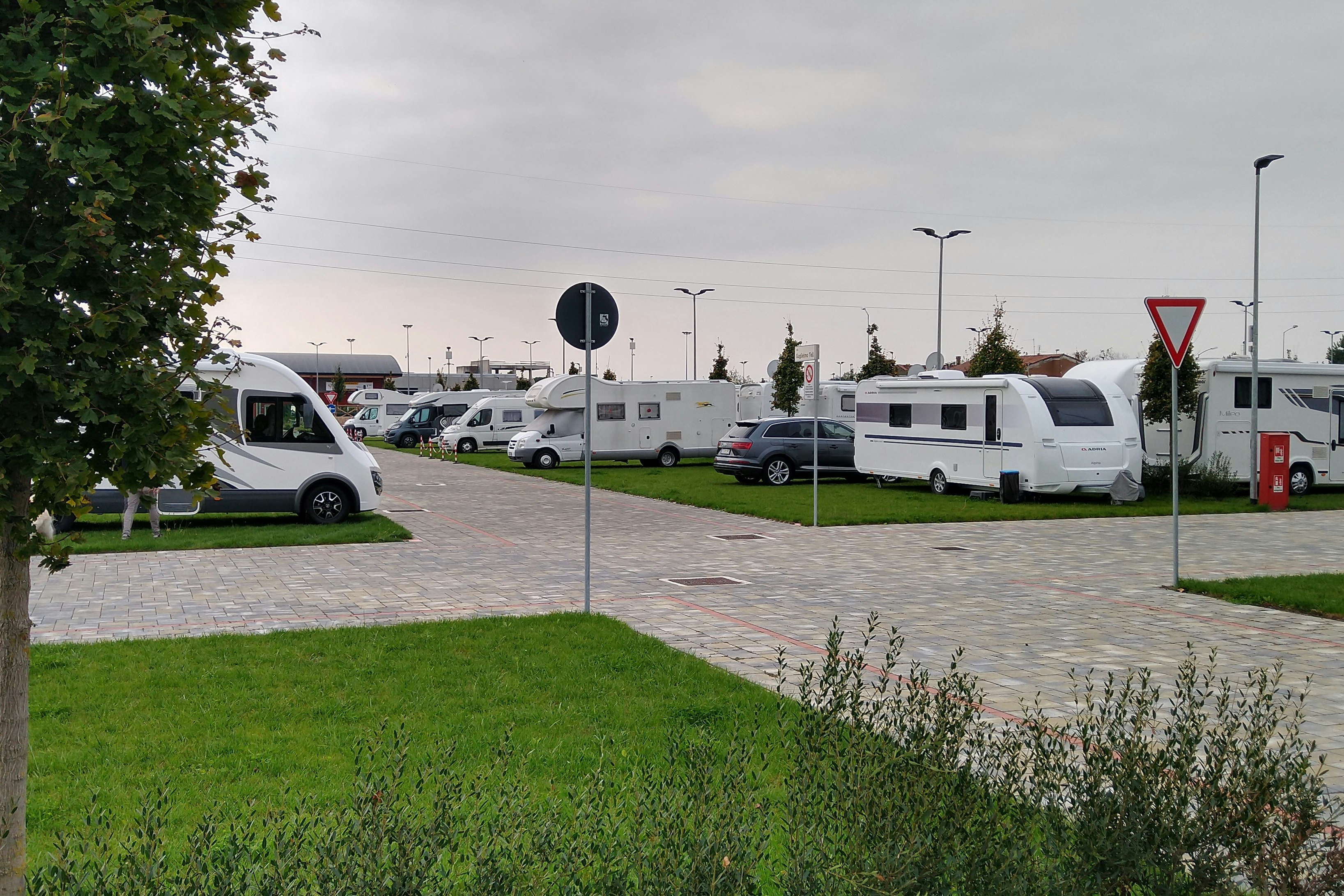 Wohnwagen und Campingbusse auf Stellplätzen, gepflasterte Wege und Rasenfläche, im Hintergrund weitere Fahrzeuge auf dem Campingplatz.