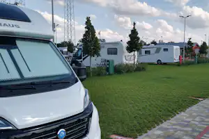 Wohnmobile auf einer Campingwiese, im Vordergrund ein Auto mit Dachzelt, daneben weitere Camper und Bäume.