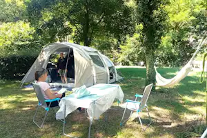 Campingzelt im Grünen mit Tisch, Stühlen und Sonnenschirm, daneben Hängematte zwischen Bäumen im Garten.