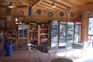 Getränke-Kühltheke und Verkaufsregal im Camping-Shop mit Holzdecke, Sitzgruppe und Regalen voller Flaschen und Dosen.